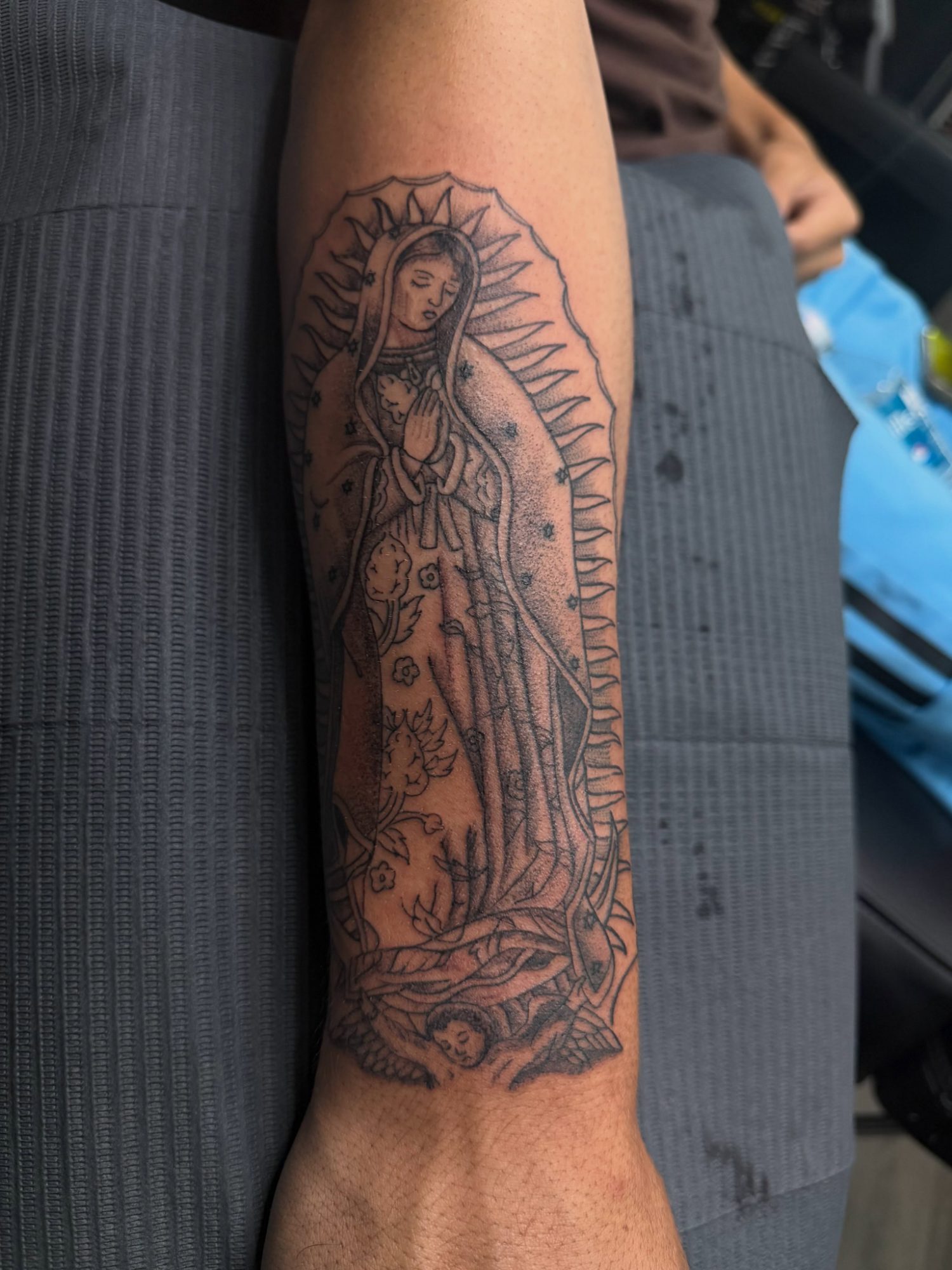 Fine line tattoo of Our Lady of Guadalupe with soft shading, on the inner forearm